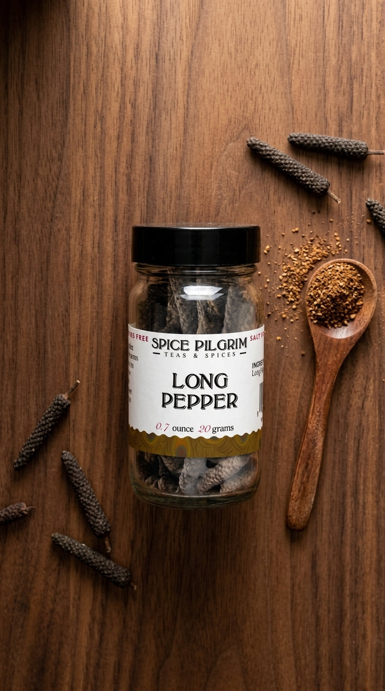 A single glass jar of long pepper sits centered on a warm walnut surface, its dark slender pods visible through clear