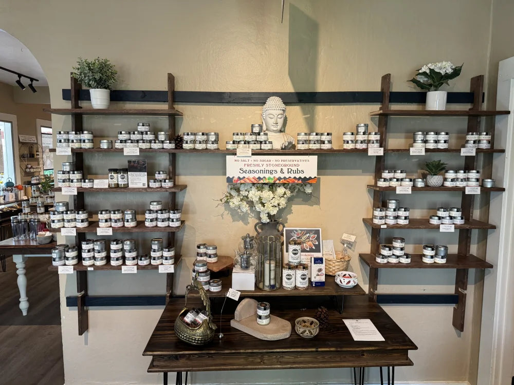 A retail display of Seasonings and Rubs arranged on dark wood floating shelves and a matching table against a beige wall.