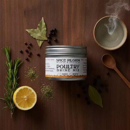 A clear glass jar of Poultry Brine Mix sits centered on a walnut surface, its aromatic blend of whole juniper berries,