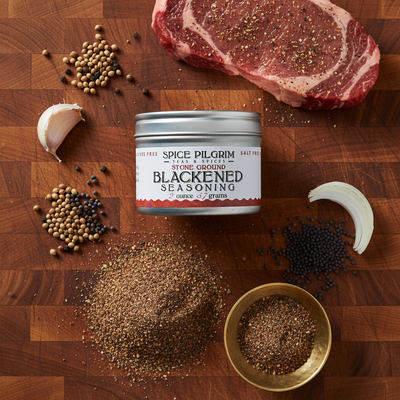 Spice Pilgrim blackened seasoning can on a wooden surface with spices and raw meat.