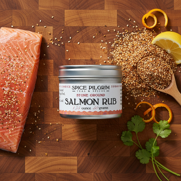 Spice Pilgrim Salmon Rub on a wooden cutting board with salmon and spices.