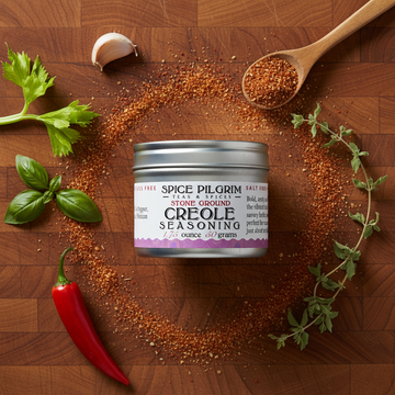 Spice Pilgrim Creole Seasoning can on a wooden surface with herbs and a pepper.