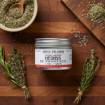 Spice Pilgrim Herbs de Provence container on a wooden surface with herbs and a bowl of spices.