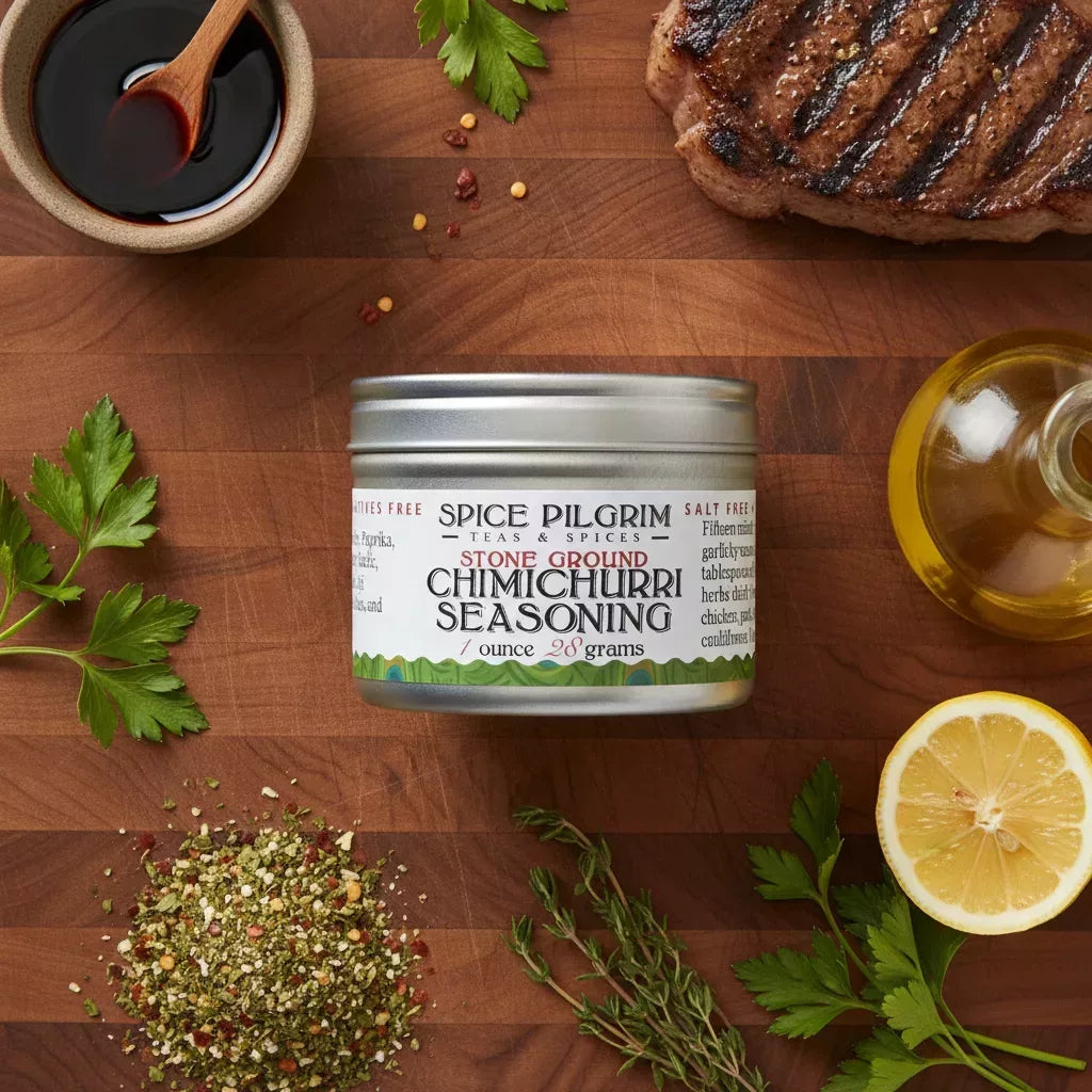 Spice Pilgrim Stone Ground Chimichurri Seasoning tin, 1 ounce, surrounded by fresh herbs, grilled steak, lemon, and olive oil on a wood cutting board