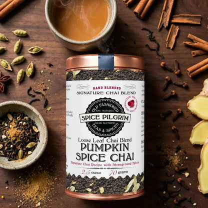 A steaming cup of brewed pumpkin chai sits center-frame on a walnut surface, the dark amber liquor catching warm light,