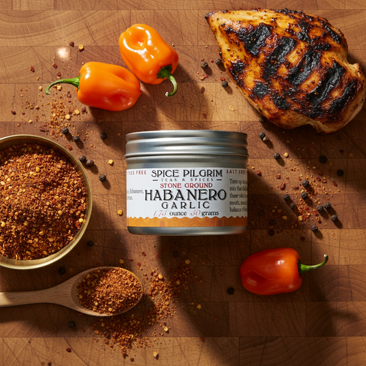 Spice Pilgrim Habanero Garlic spice jar on a wooden surface with habanero peppers and garlic.