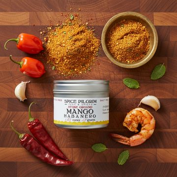 Spice Pilgrim Mango Habanero spice container on a wooden cutting board with peppers, garlic, and a shrimp.