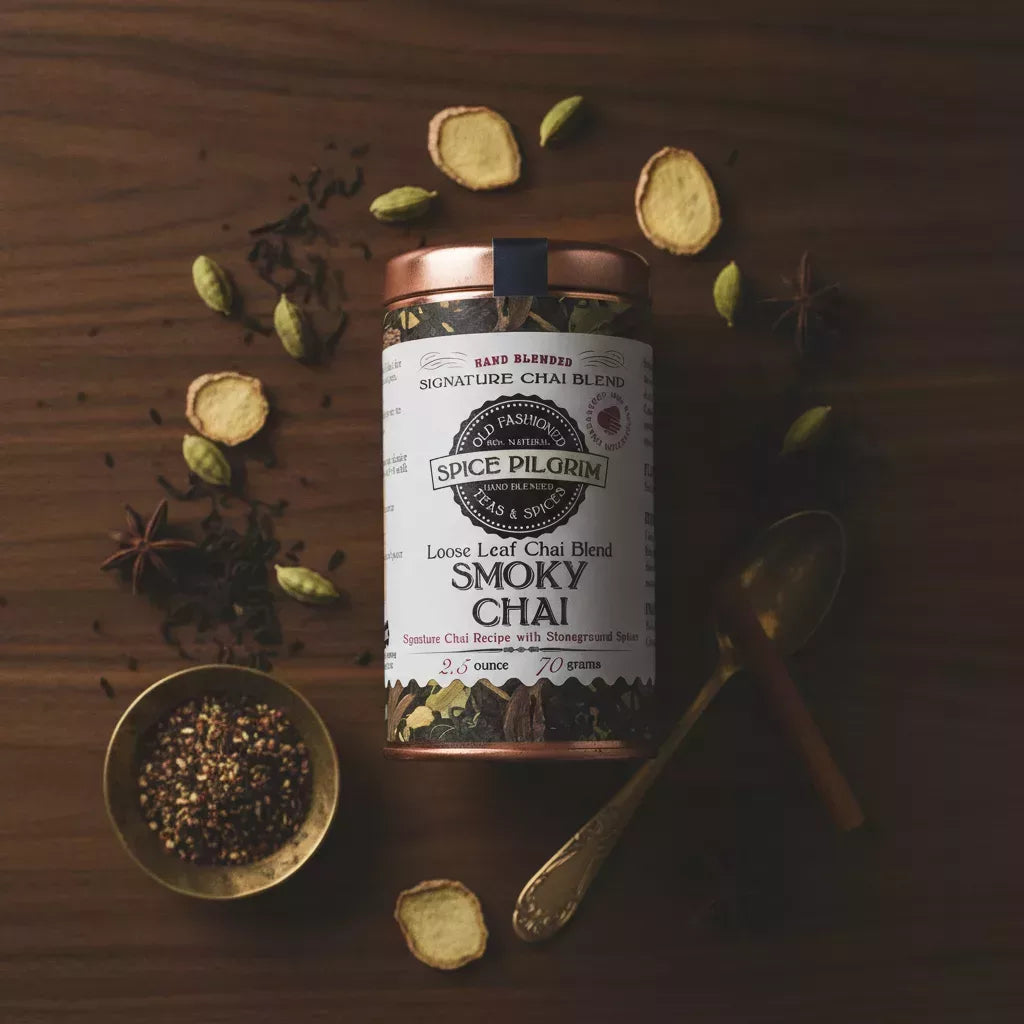 Spice Pilgrim Smoky Chai loose leaf chai blend tin, surrounded by cardamom, star anise, and ginger slices on a wooden surface