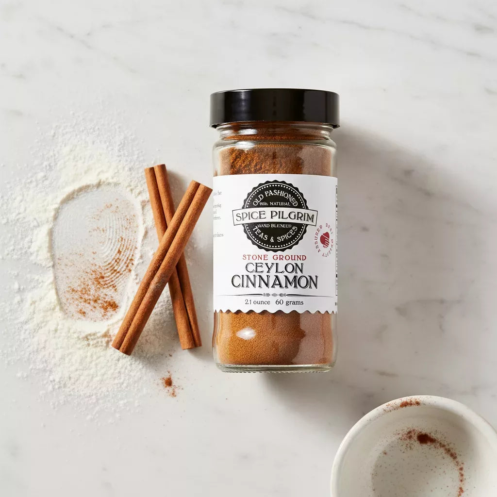 An open jar of stone-ground Ceylon cinnamon sits on a white marble surface beside a small ceramic mixing bowl dusted