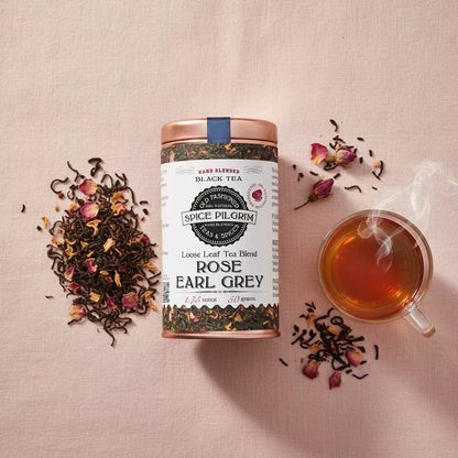 Rose Earl Grey tea tin on rose linen cloth, loose tea leaves scattered artfully, glass teacup with steeped amber tea