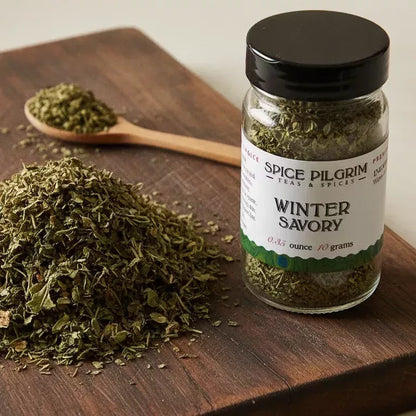 Spice Pilgrim Winter Savory dried herb jar beside a loose pile of the herb and a wooden spoon on a cutting board
